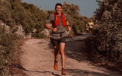 Coureur de trail courant sur un sentier ensoleillé, équipé d’un gilet rouge